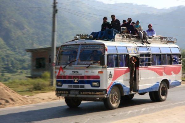 Riding a bus in Nepal, with people sitting on top and hanging out the side; photo by Sherry Ott of Ottsworld